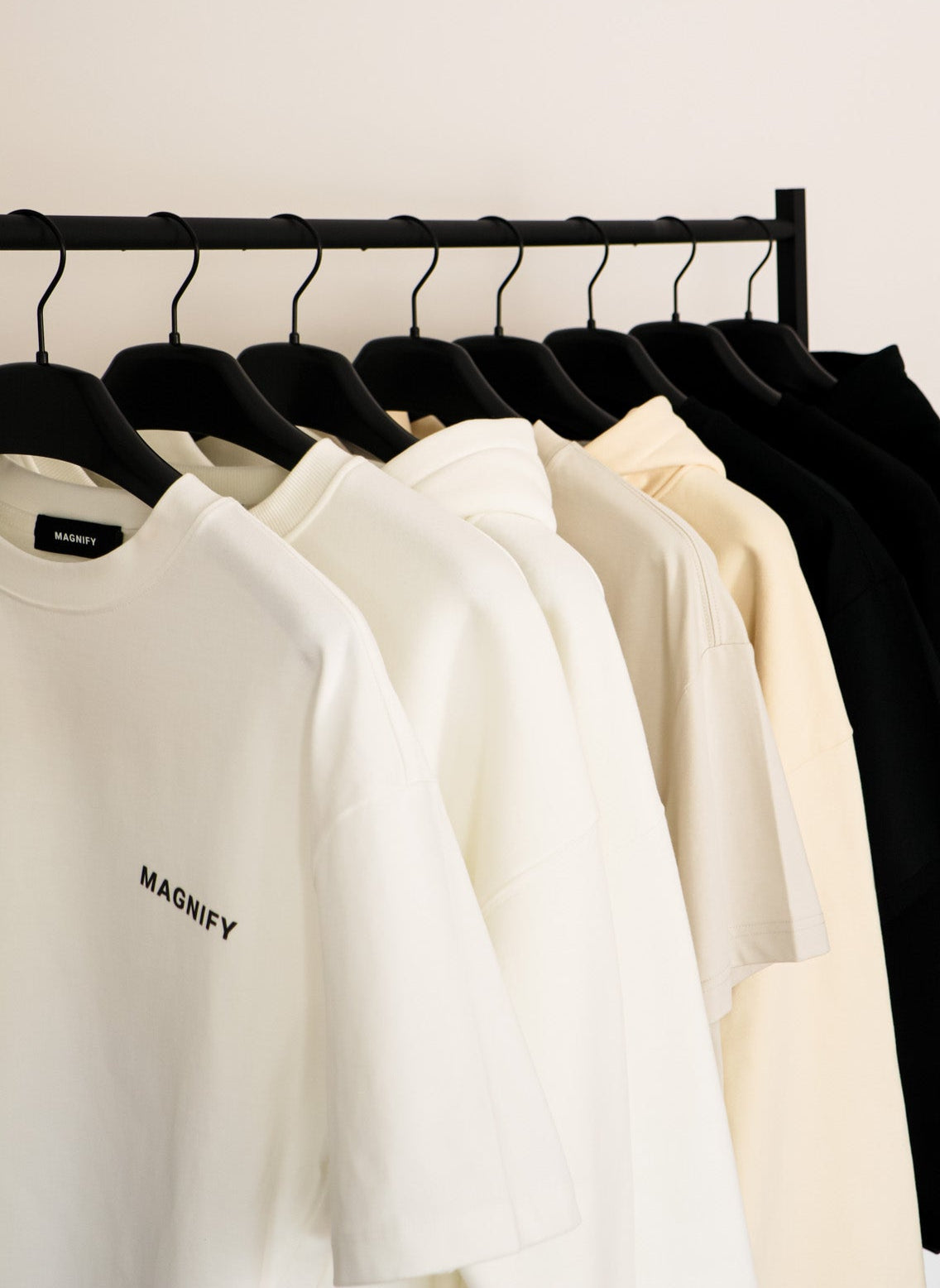 White sweatshirt with 'MAGNIFY' logo on a rack with other clothes.