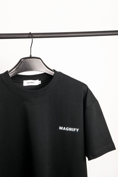 Black t-shirt with 'MAGNIFY' logo on a hanger against a white background