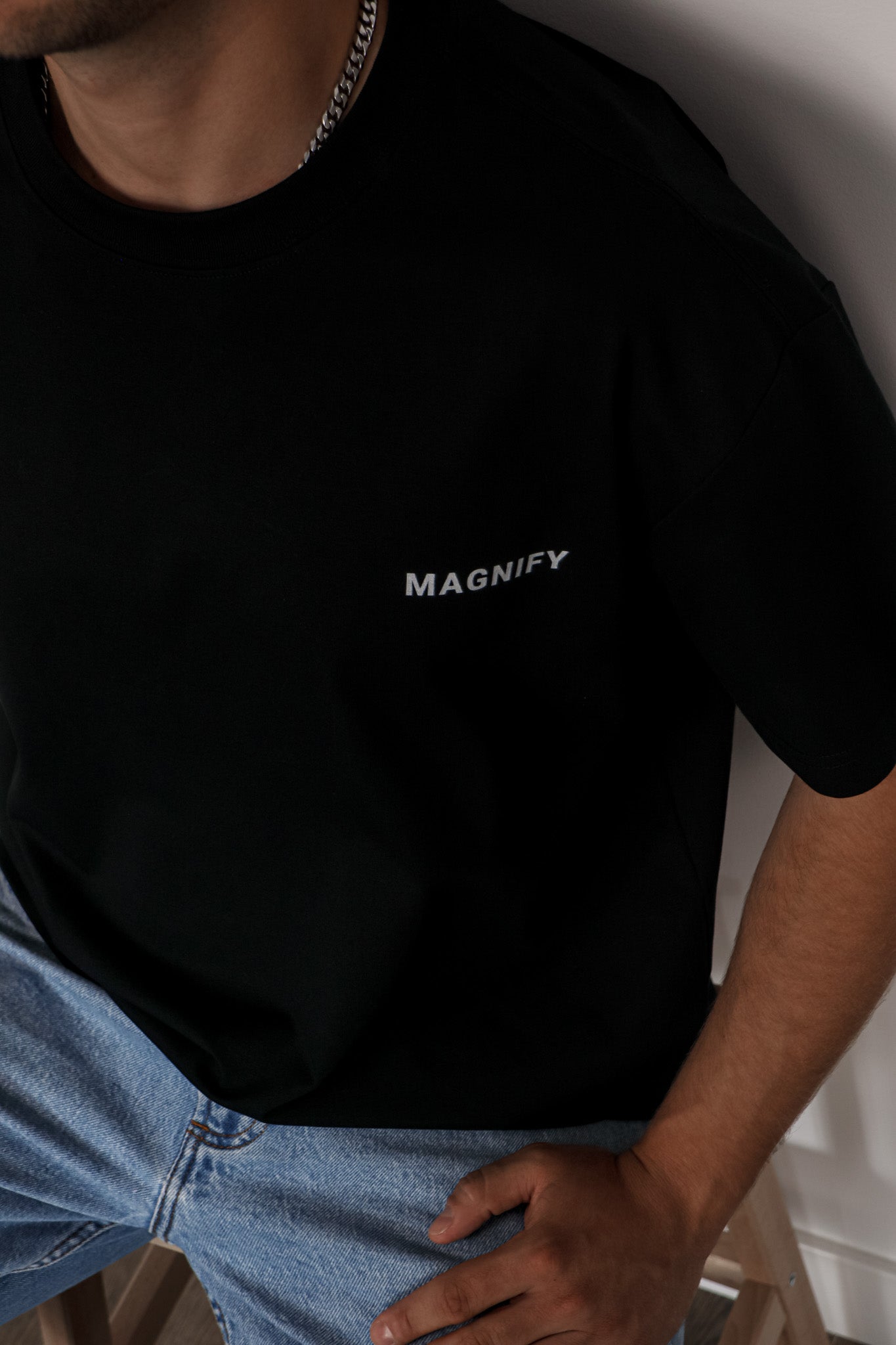 Person wearing a black t-shirt with 'MAGNIFY' text, standing against a neutral background.