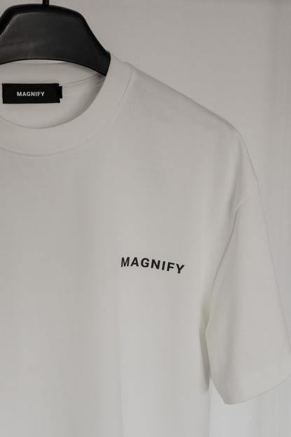 White t-shirt with 'MAGNIFY' logo on a hanger against a white background