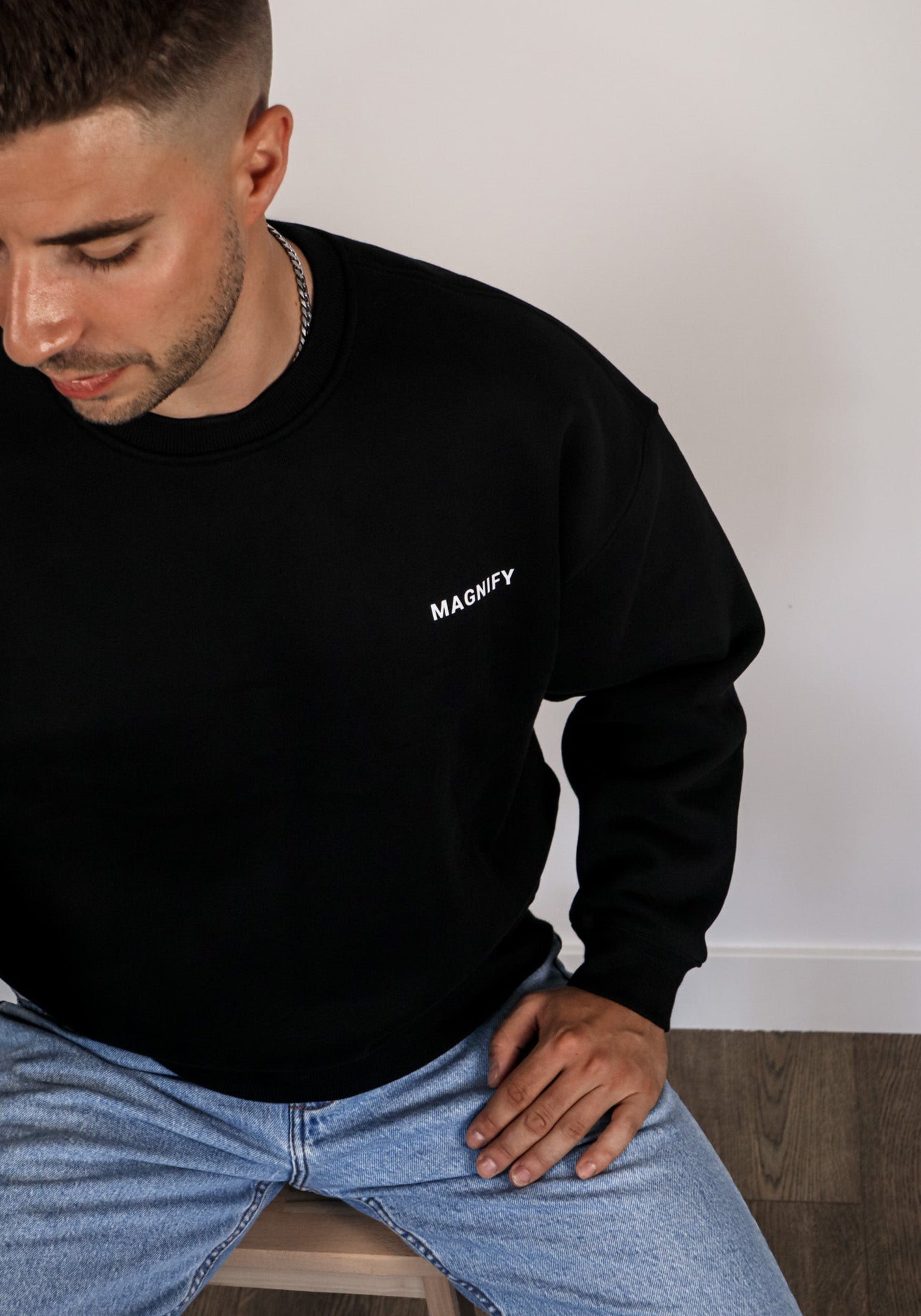 Man wearing a black sweatshirt with 'MAGNIFY' logo sitting on a chair.