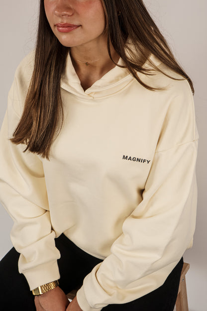 Person wearing a beige hoodie with 'MAGNIFY' text on a neutral background