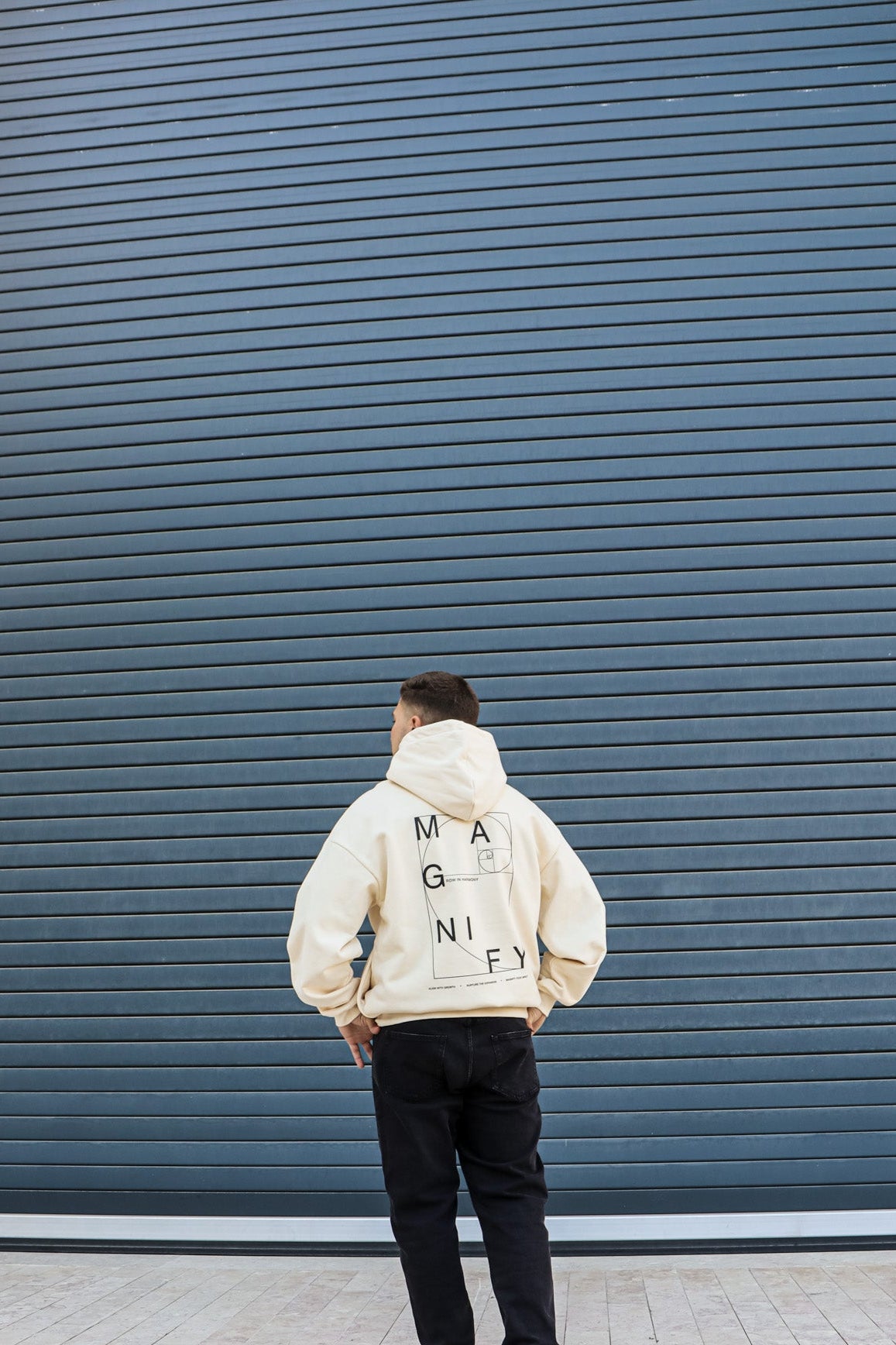 Person wearing a beige hoodie with text standing against a blue wall