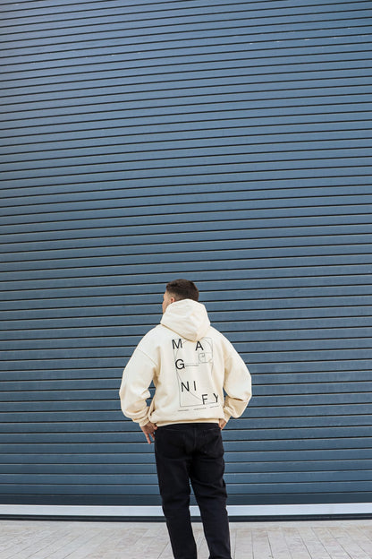 Person wearing a beige hoodie with text standing against a blue wall