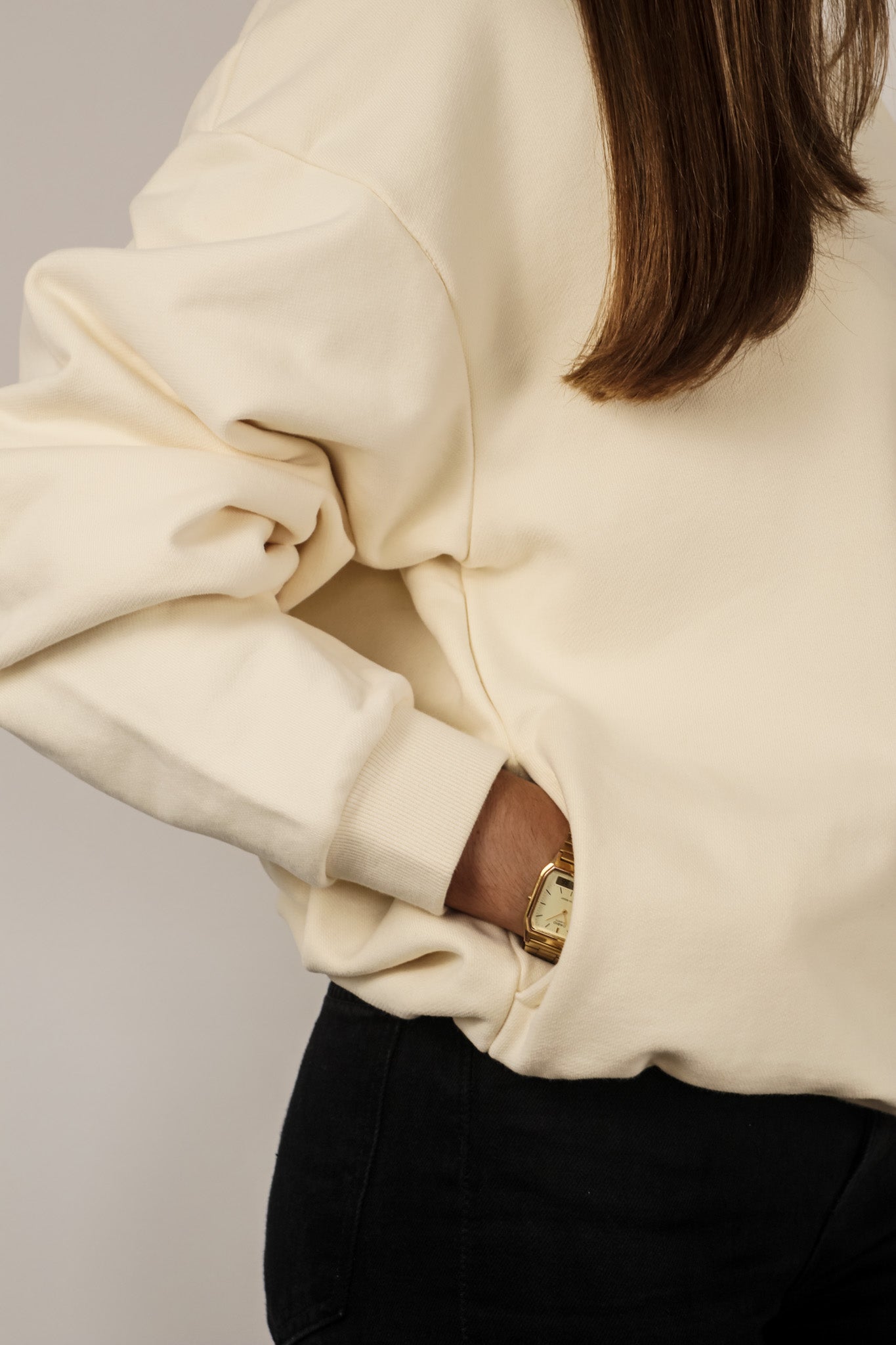 Person wearing a beige sweatshirt with a gold zipper detail on a plain background