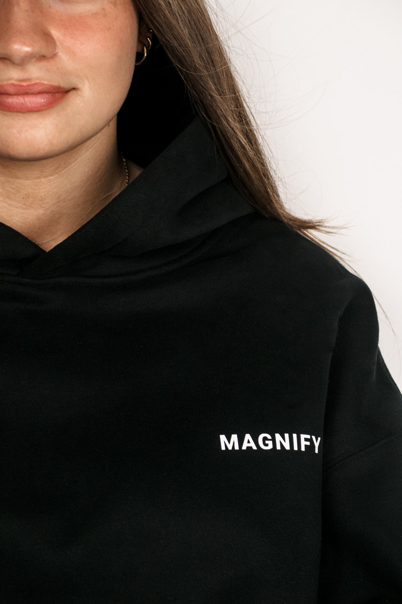 Person wearing a black hoodie with 'MAGNIFY' text on a plain background