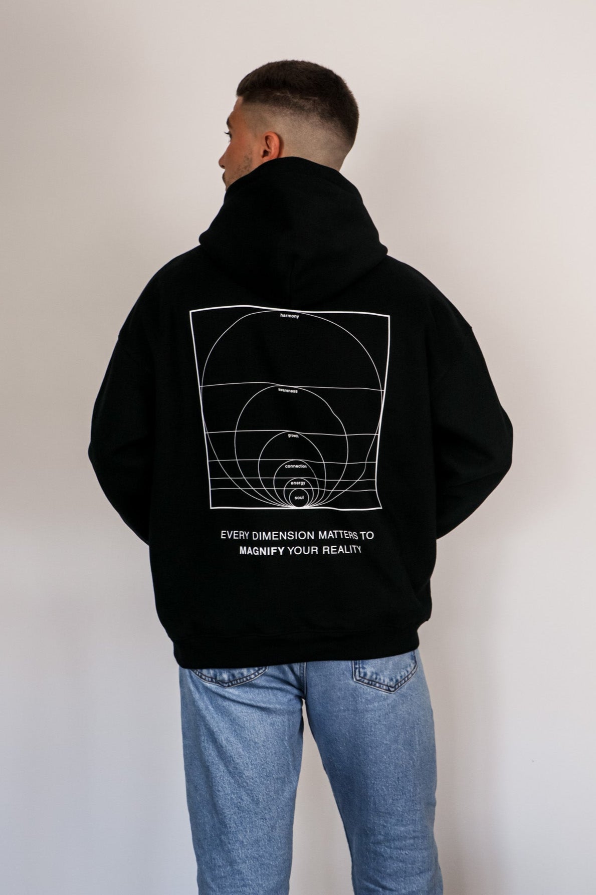 Person wearing a black hoodie with a design and text on the back, standing against a plain background
