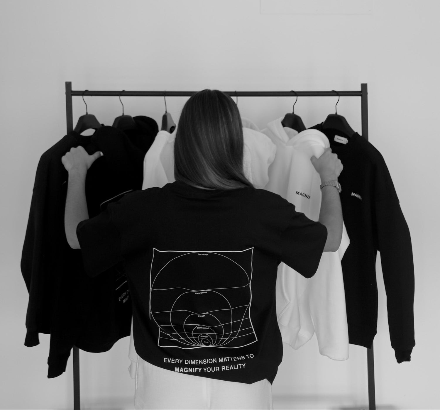 Person wearing a black jacket with text and graphics, standing in front of a rack of clothes.