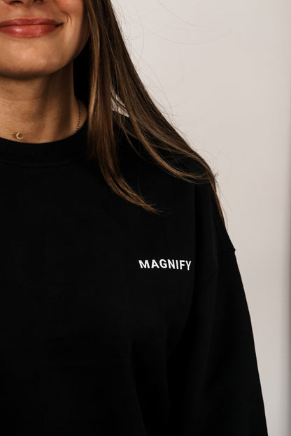 Person wearing a black shirt with 'MAGNIFY' text on a plain background