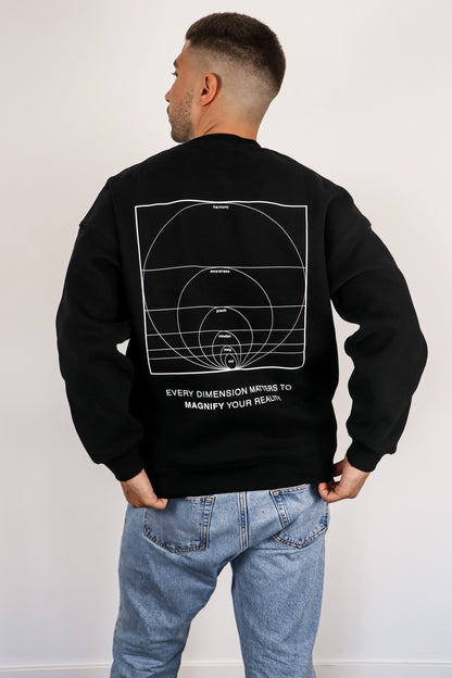 Person wearing a black sweatshirt with a geometric design on the back, standing against a white wall.
