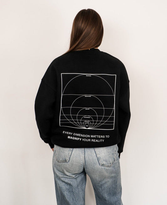 Person wearing a black sweatshirt with white graphics and text on the back, standing against a plain background.