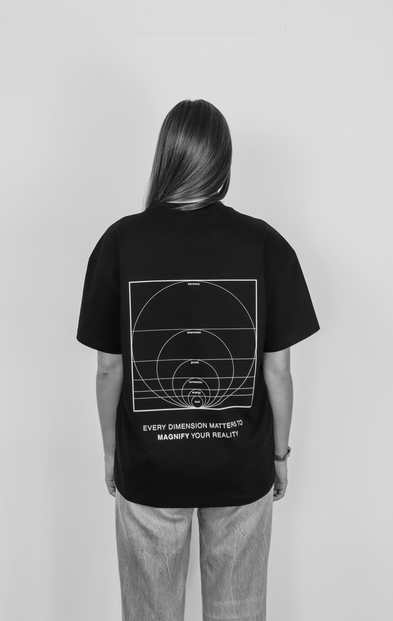 Person wearing a black t-shirt with a design and text on the back, standing against a plain background.