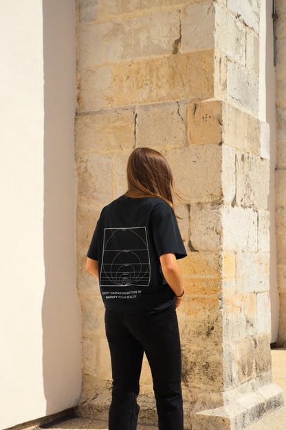 Person wearing a black t-shirt with a geometric design, standing against a stone wall.
