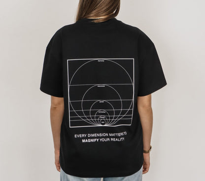 Person wearing a black t-shirt with geometric design and text on the back, on a plain background