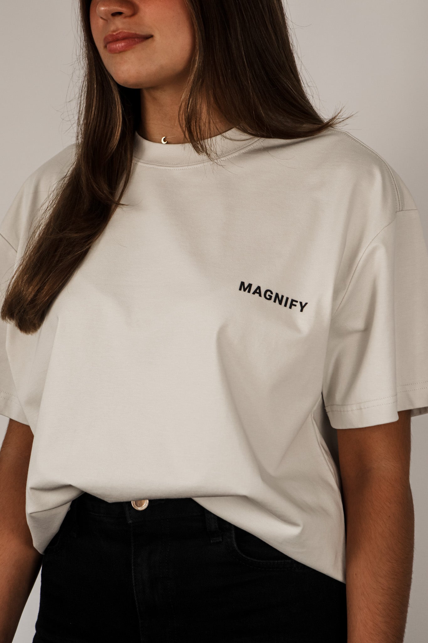 Person wearing a light gray t-shirt with 'MAGNIFY' logo on a plain background