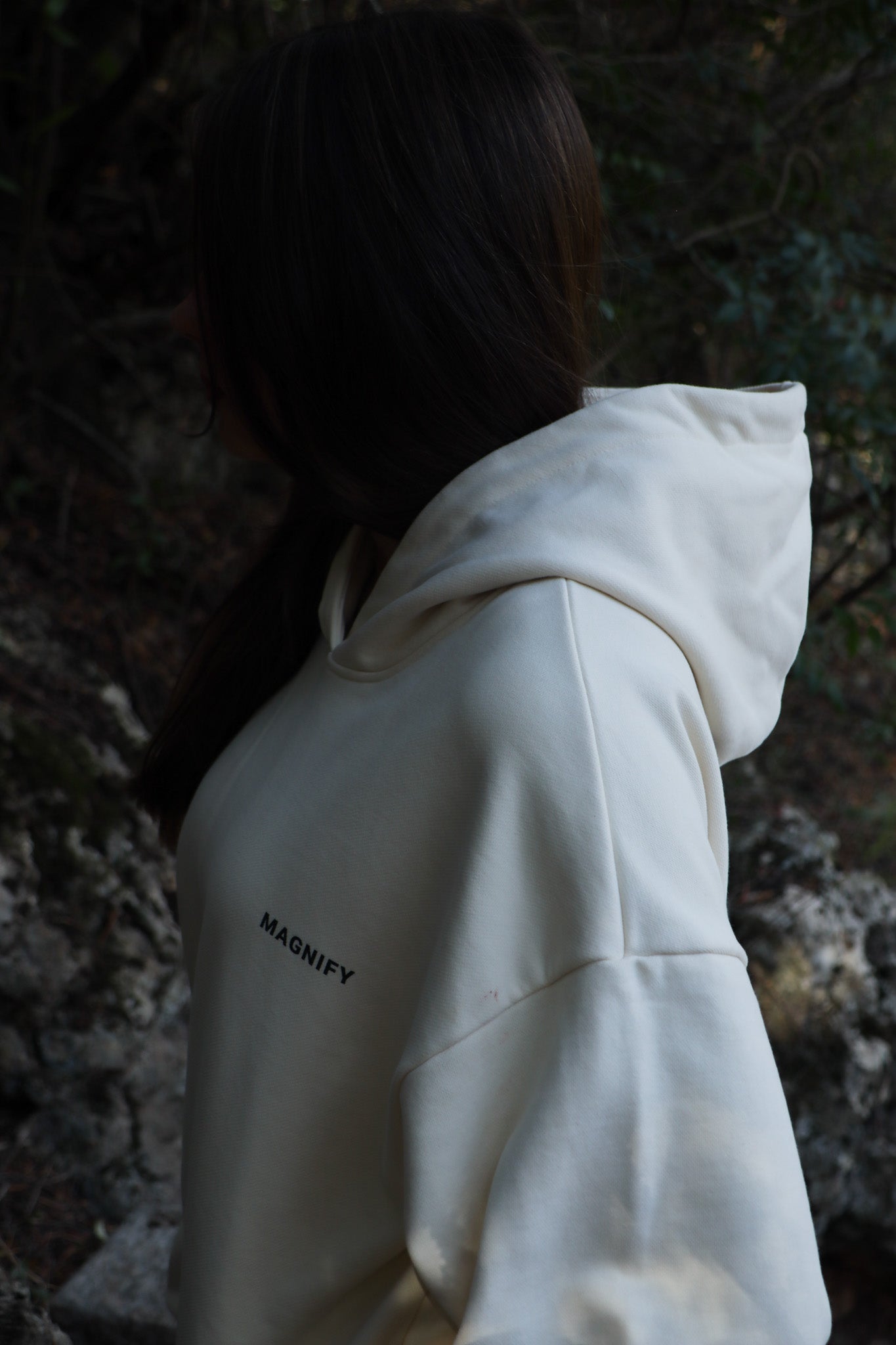 Person wearing a white hoodie with 'Mackey' branding in a forest setting