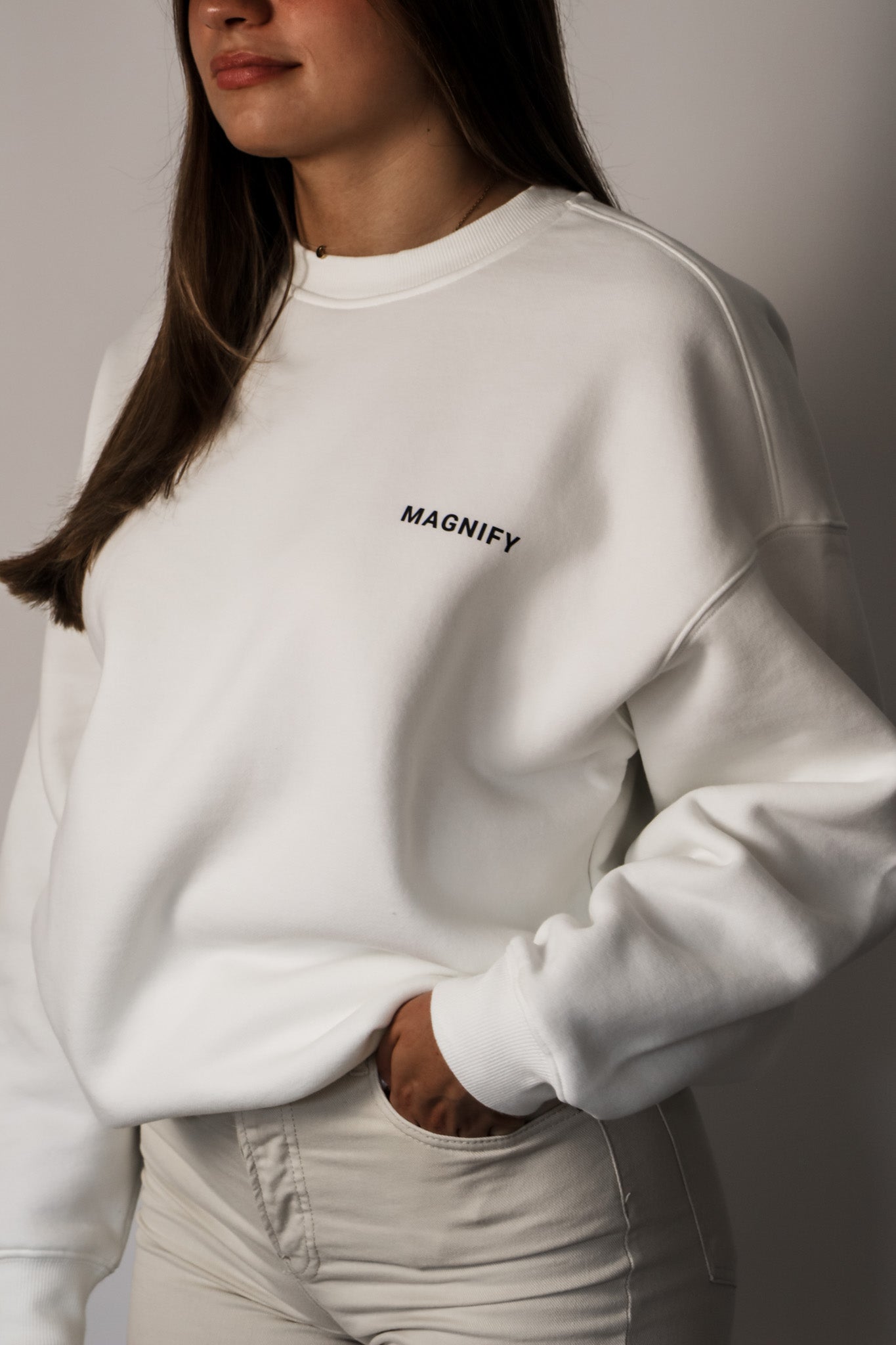 Person wearing a white sweatshirt with 'MAGNIFY' text on a plain background