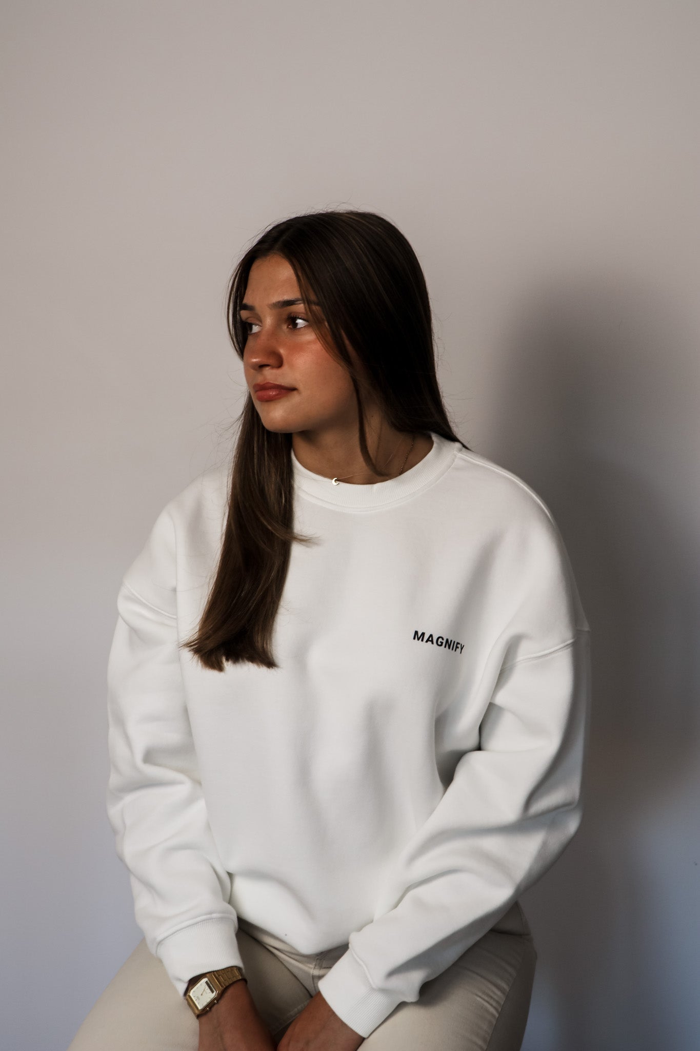 Person wearing a white sweatshirt with a logo against a plain background