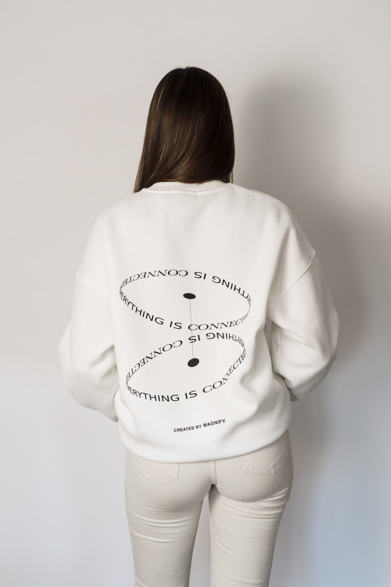 Person wearing a white sweatshirt with text design on the back against a plain background
