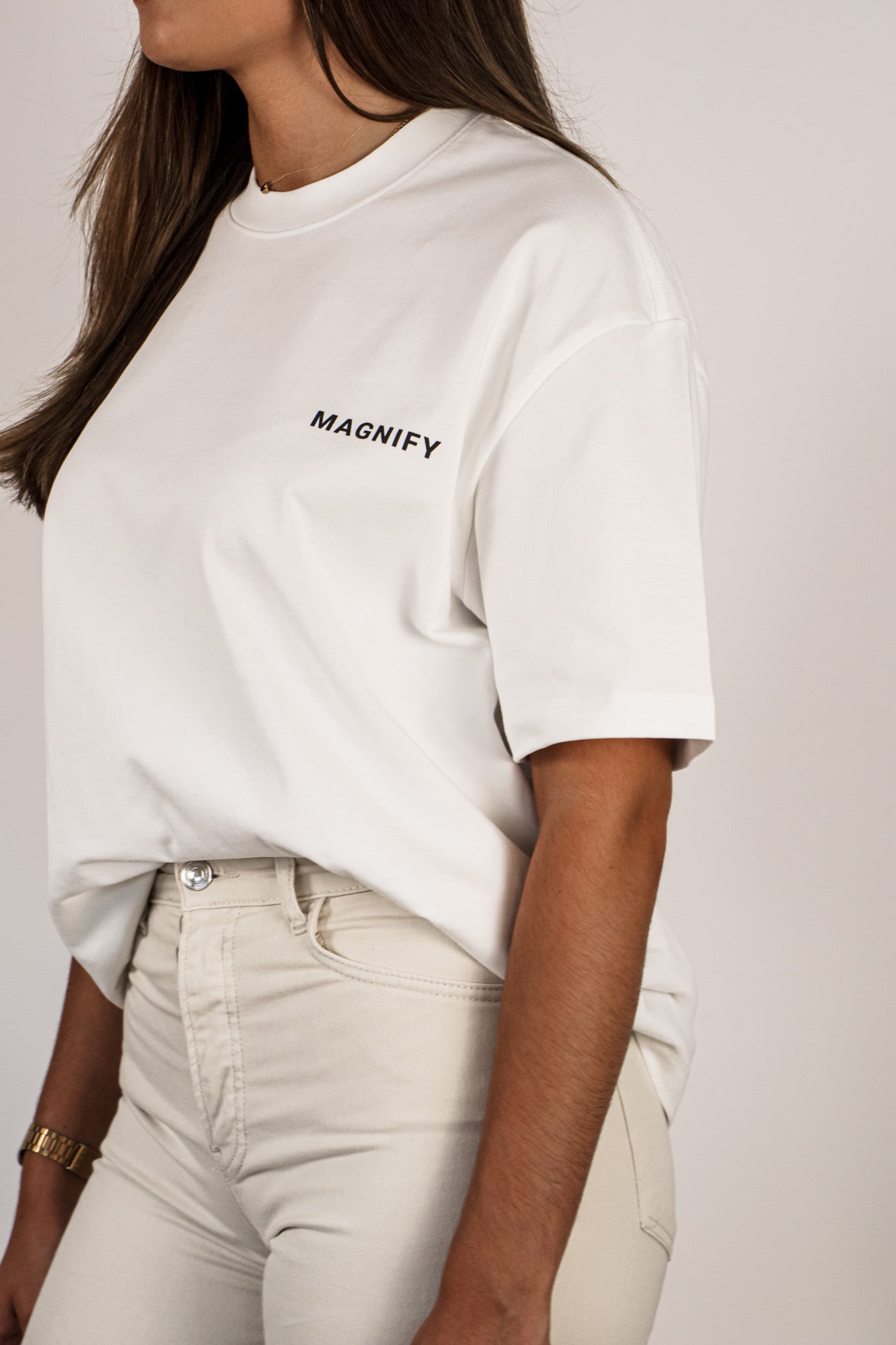 Person wearing a white t-shirt with 'MAGNIFY' text on a plain background