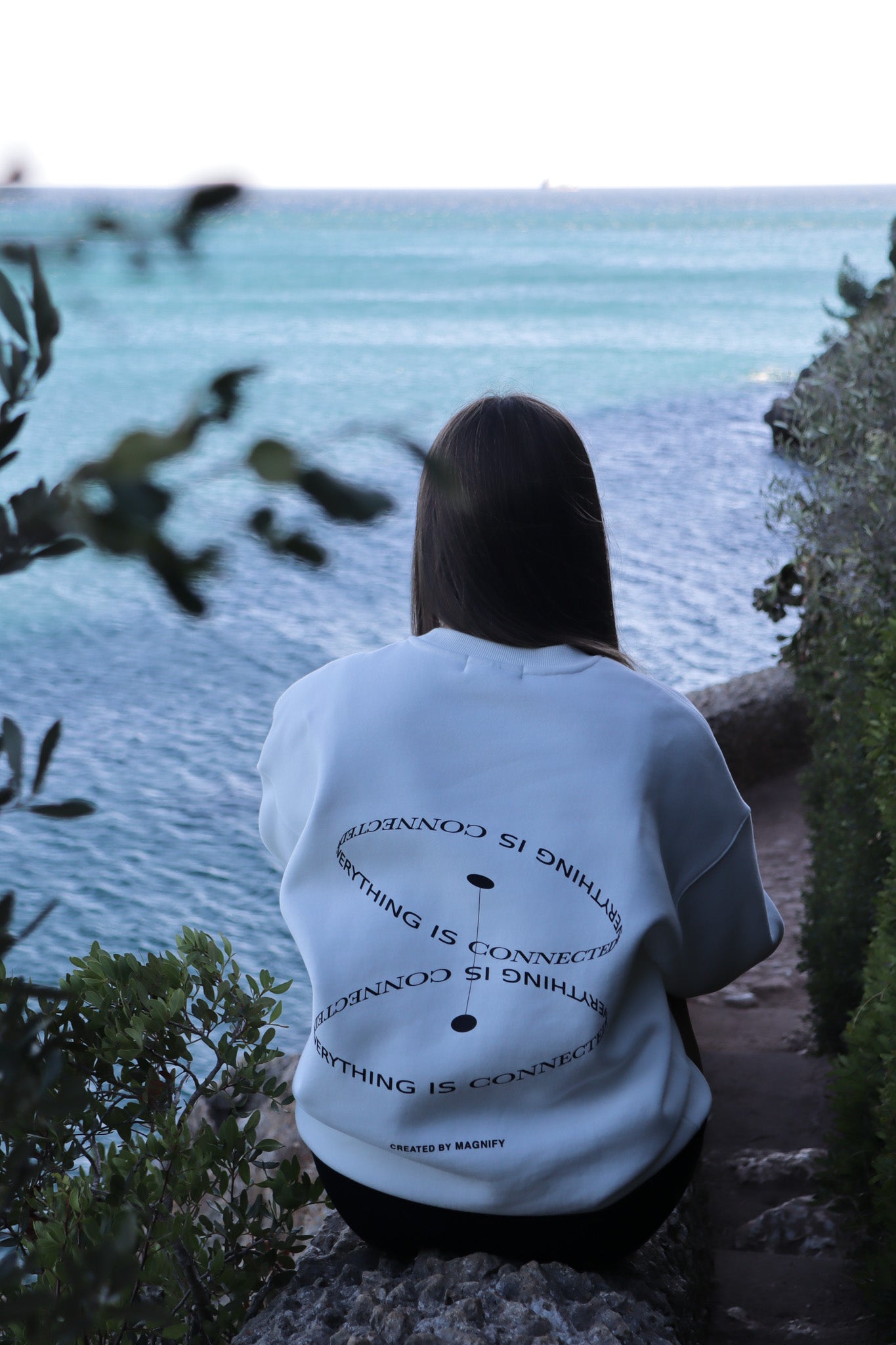 Person wearing a white t-shirt with text sitting by a body of water.