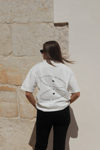 Person wearing a white t-shirt with text, standing against a stone wall.