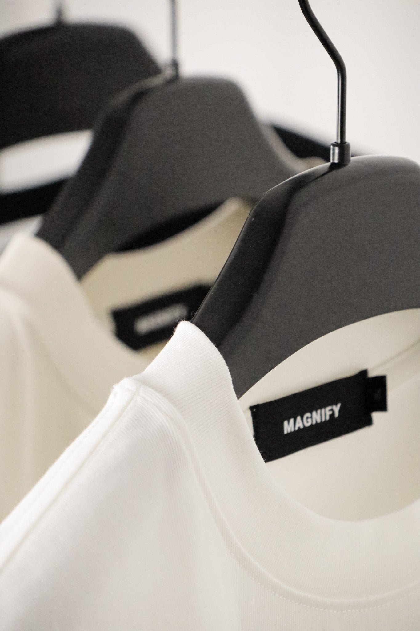 White shirt on a black hanger with 'MAGNIFY' label against a blurred background