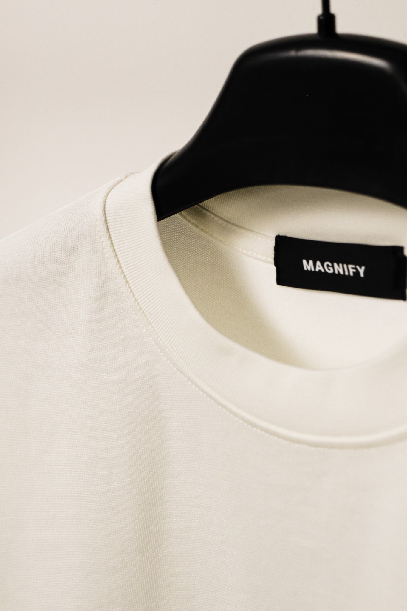 White shirt on a black hanger with 'MAGNIFY' label against a light background