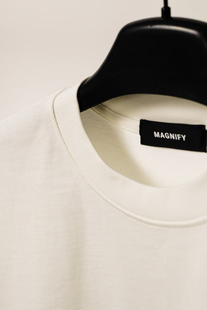 White shirt on a black hanger with 'MAGNIFY' label against a light background