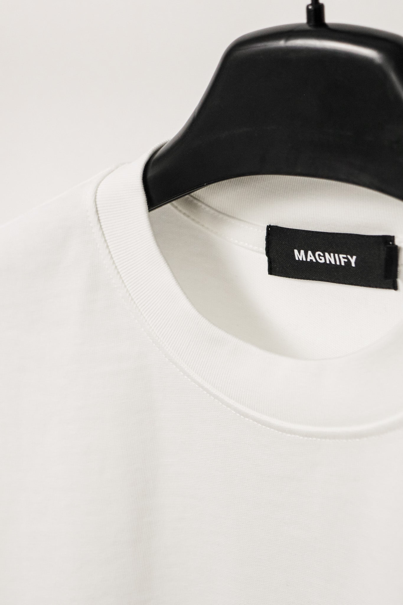 White shirt with a 'MAGNIFY' label on a black hanger against a white background