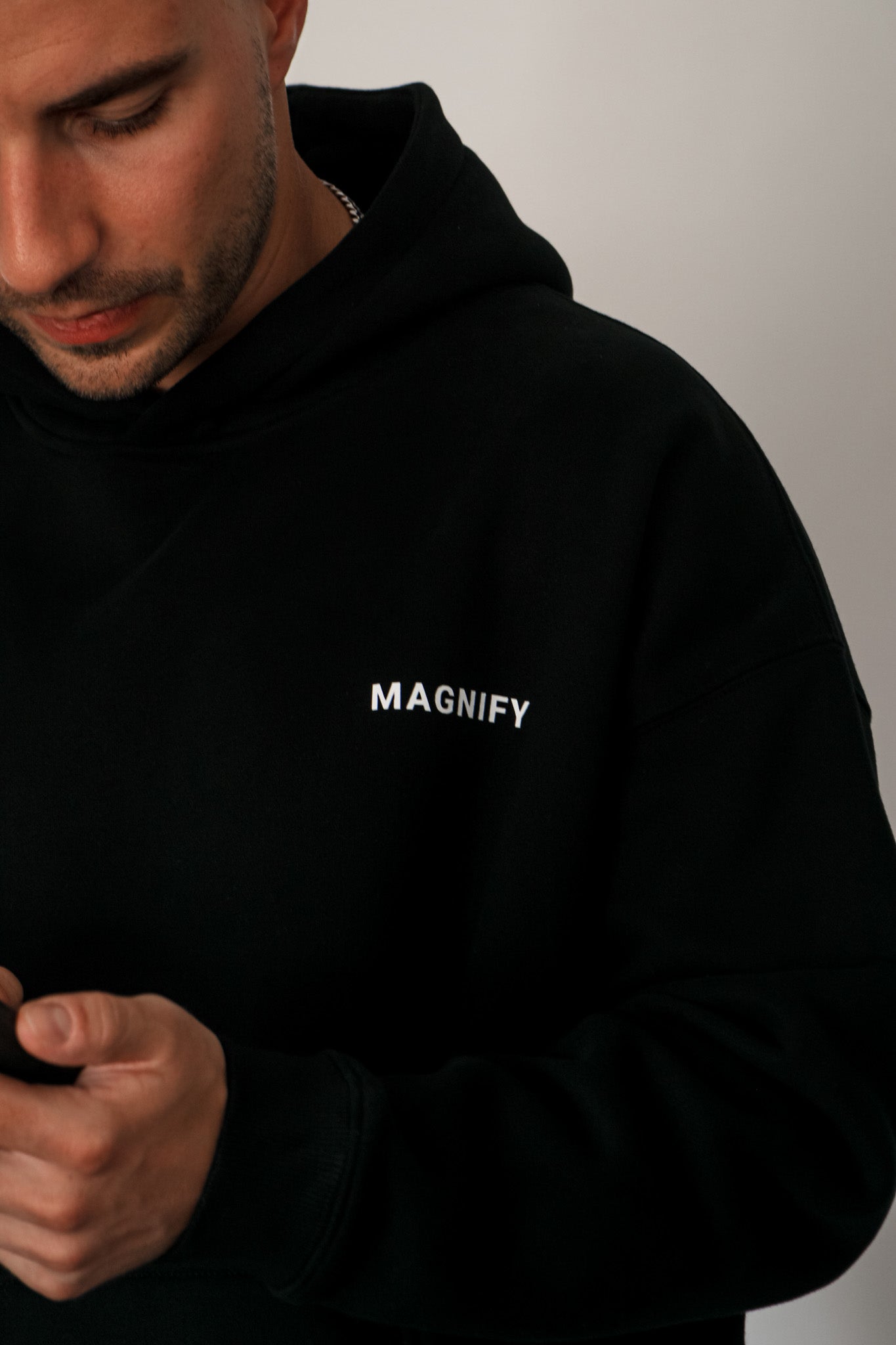 Man wearing a black hoodie with 'MAGNIFY' text on a plain background