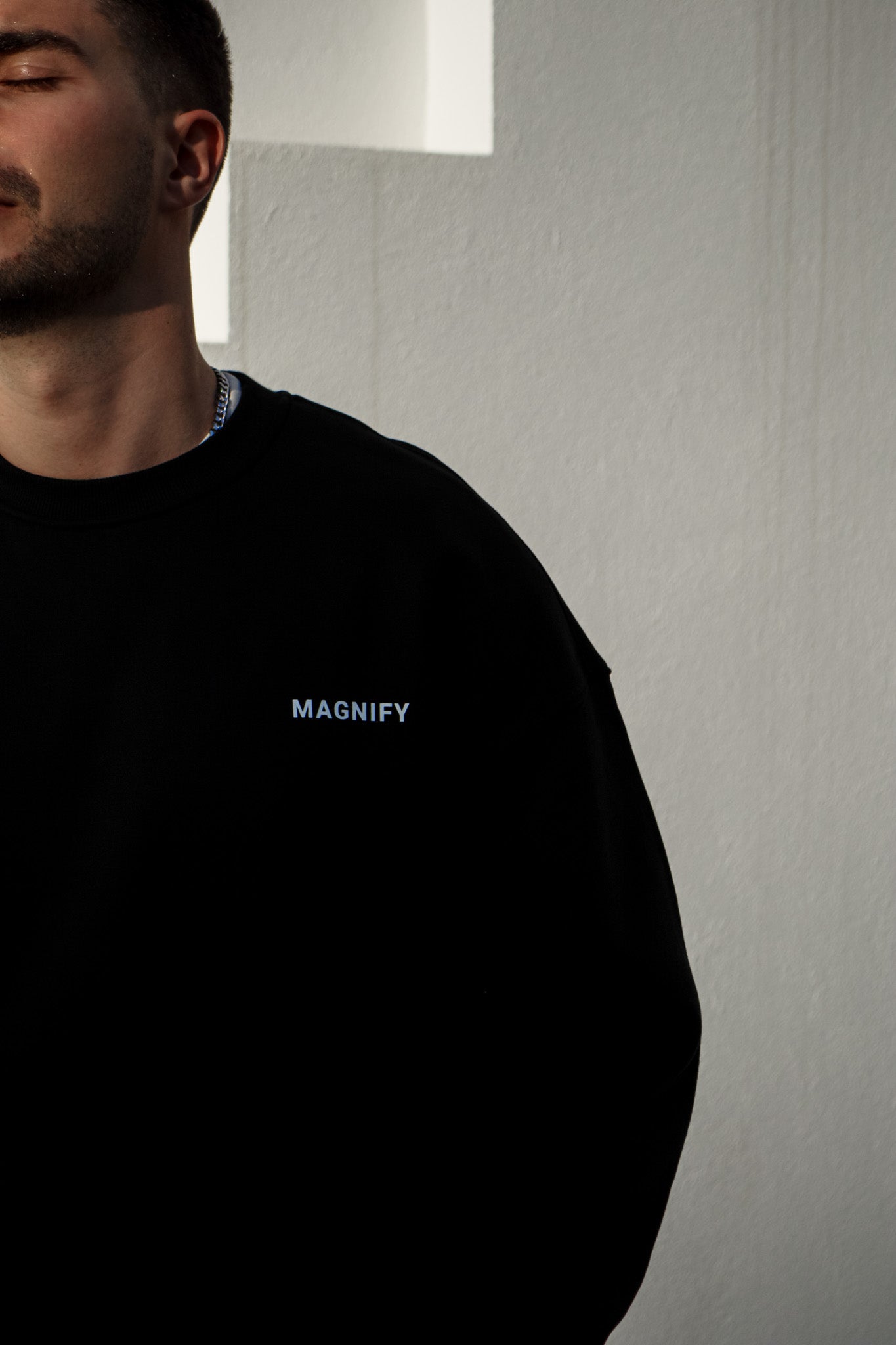 Person wearing a black sweatshirt with 'MAGNIFY' logo against a neutral background