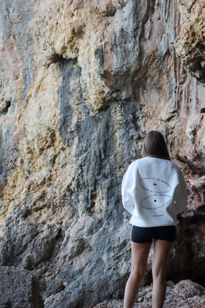 Person wearing a white sweatshirt with text standing against a rocky cliff.